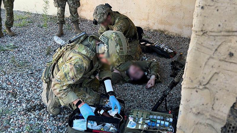 Special operations first aid course participants assess a casualty role-player and prepare for field medical care under the supervision of Australian and American directing staff.