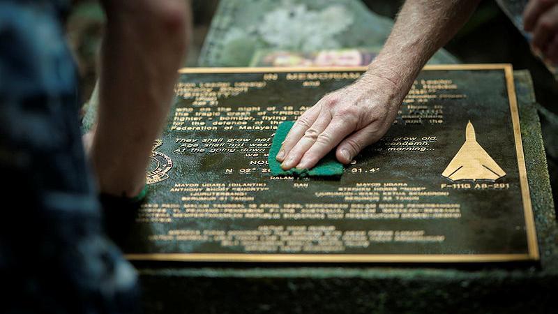Wing Commander David Riddel and Cameron Kelly clean the memorial plaque at the crash site