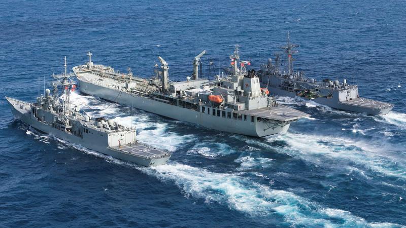 HMAS Sirius refuels HMAS Darwin (left) and HMAS Melbourne (right) simultaneously while underway, at the same time a MRH-90 Taipan helicopter conducts a vertical replenishment off the northern Australian coast in 2017. 