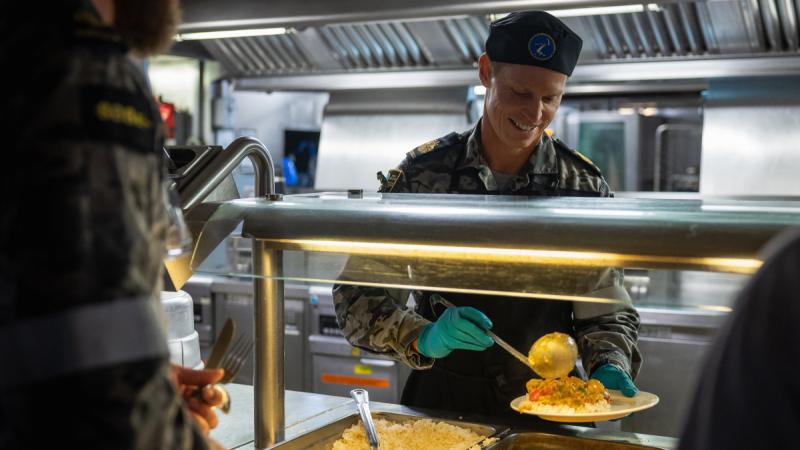 Navy Warrant Officer Dion Blair, HMAS Adelaide Command Warrant Officer, serves dinner to the ship's company in the HMAS Adelaide galley. 