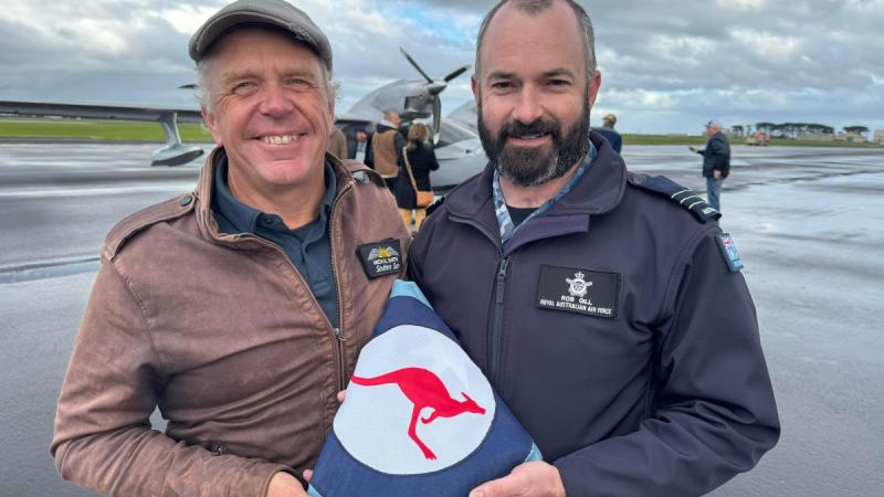Mr Micheal Smith presents the Royal Australian Air Force ensign that completed the re-enactment journey with him to Wing Commander Rob Gill, Commanding Officer of 21 Squadron.