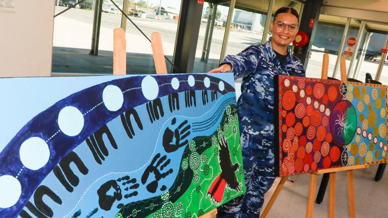 Air Force Aircraftwoman Dakoda Dalton with two pieces of artwork she painted and is presenting to be displayed in her workplace, 13 Squadron Air Movements RAAF Base Darwin, as part of National Reconciliation Week 2024.