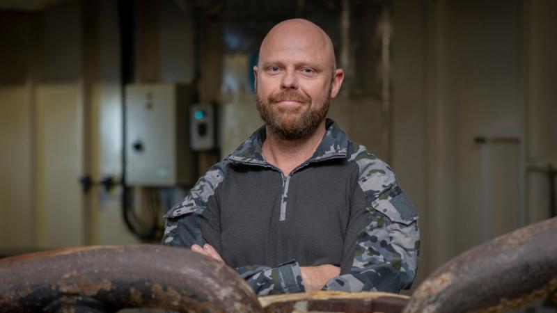 Navy HMAS Adelaide's ship's husbandry manager Petty Officer Thomas Archer next to the ship’s cable and anchor. 