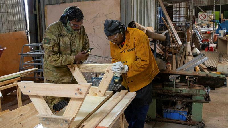 Private Luke Kennedy assists a fellow Amata community member with the construction of a bench seat.