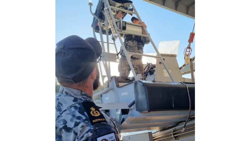 Royal Australian Navy sailors work onboard HMNZS Manawanui with Royal New Zealand Navy sailors to repair a rigid-hulled inflatable boat.