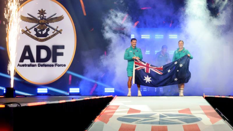 Team Australia captains, Sergeant Emily Lahey (right) and Cooper Blackwood carry the Australian National Flag as they lead the Australian contingent competing at the Warrior Games 2024 on to the stage for the closing ceremony.