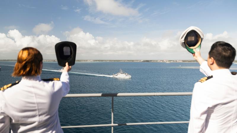Ships company from HMAS Choules cheer ship as Guardian Class patrol boat VOEA Ngahau Koula, carrying His Majesty King Tupou VI of Tonga, passes by during an International Fleet Review to celebrate the 50th anniversary of the Tonga Royal Navy.