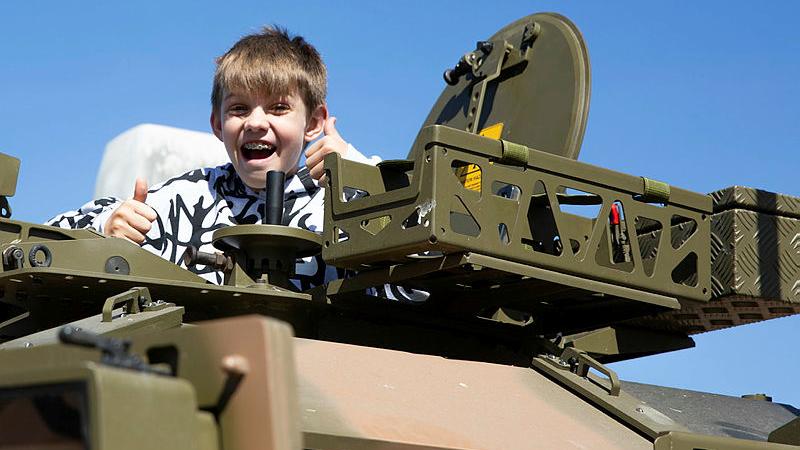 Australian Army soldiers from 11th Brigade invite a young show-goer to climb up through the roof hatch of a Hawkei light protected mobility vehicle at the Cairns Show during Exercise Austral Shield 2024. 