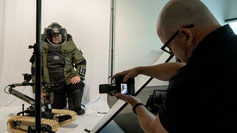 Sergeant Damian Dickson kneels while wearing an explosive ordnance disposal suit as Army veteran Mr Michael Glass captures portraits for his final TAFE assessment at RAAF Base Amberley, Ipswich. 