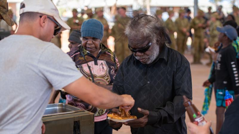 Army soldier Corporal Alexander Kurdyukov serves a BBQ lunch to Amata community member Adrian Riley at the closing ceremony for the 2024 Army Aboriginal Community Assistance Program in Amata, South Australia. 