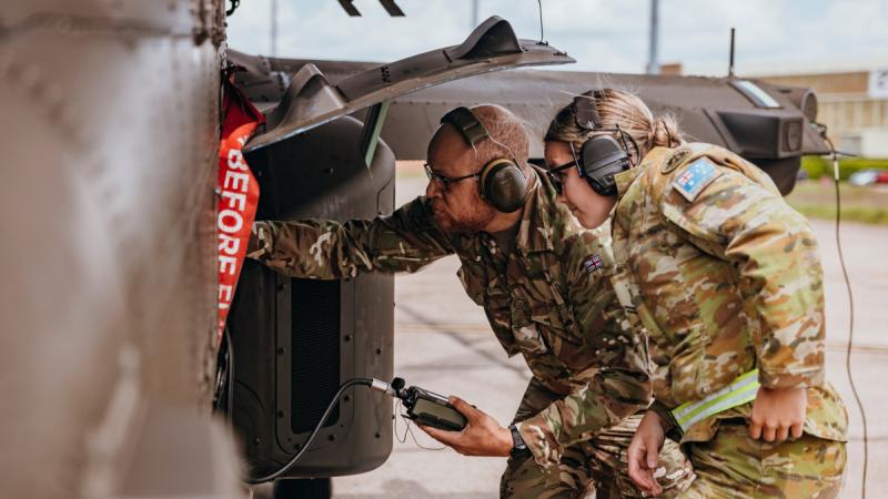 A British soldier from 3 Regiment Army Air Corps and his counterpart from the 1st Aviation Regiment, Australian Army Aviation Command, load mission planning data into the aircrafts software of a AH-64E attack helicopter.