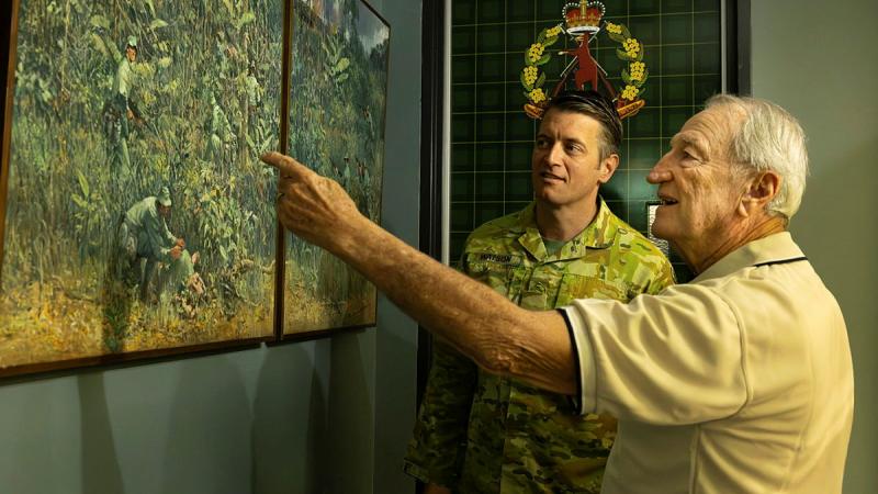 Lieutenant Colonel Ben Watson appreciates a painting of the 9th Battalion, The Royal Australian Regiment, in Vietnam with Veteran Dan Penman, right, at Gallipoli Barracks, Enoggera.