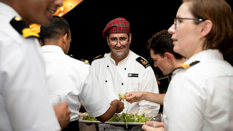 Royal Australian Navy’s Petty Officer Troy Wenman serves appetisers during an official reception on the flight deck of HMAS Stuart as part of the shore phase of Exercise Malabar. 