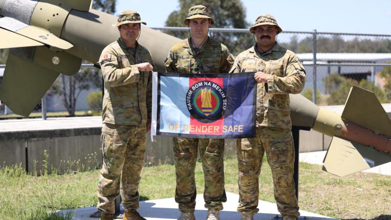 Australian Army soldiers Warrant Officer Class Two Brett Hitchins, left, Captain Johan Cillie and Sergeant Noah David hold an Operation Render Safe flag at RAAF Base Amberley in Queensland.