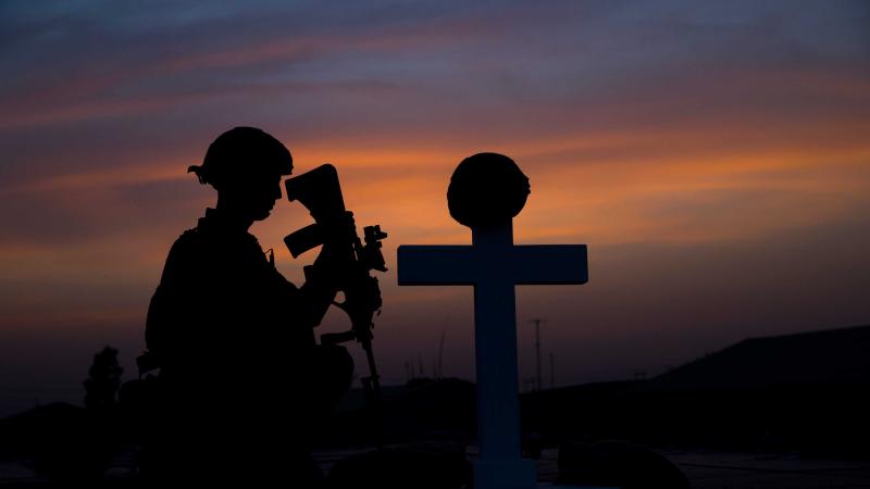 A soldier reflects at a graveside marked with a pith helmet.