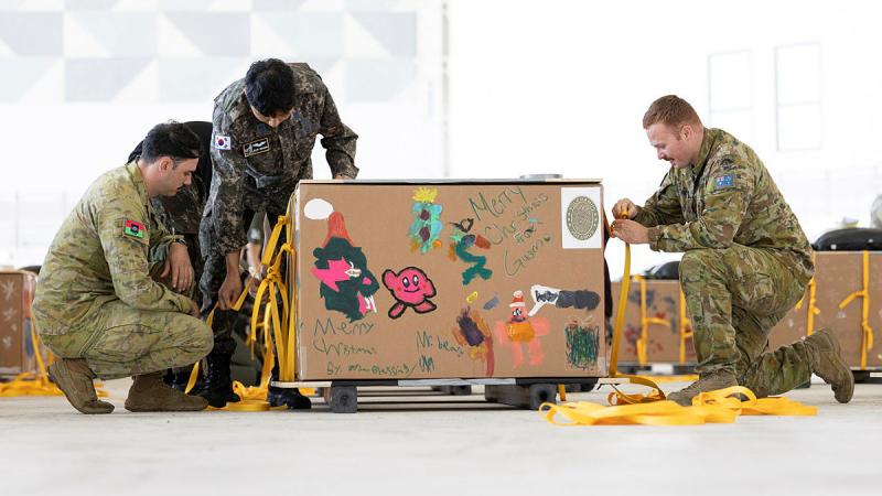 A member from the Republic of Korea Air Force, centre, helps Australian Army air dispatchers Corporal Ryan Cheevers and Private Kurt Matthews prepare a 'bundle' for Operation Christmas Drop 24.