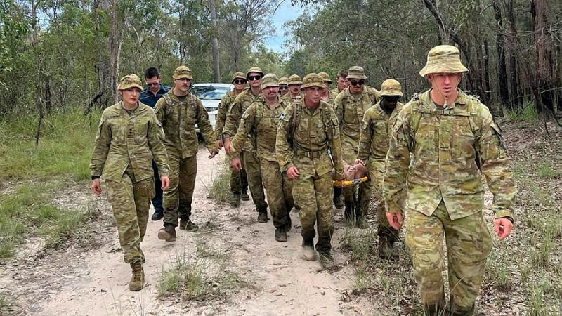 ADF Members and Queensland Ambulance Service personnel stretcher a missing man through bushland and flooded waters to emergency service vehicles. 