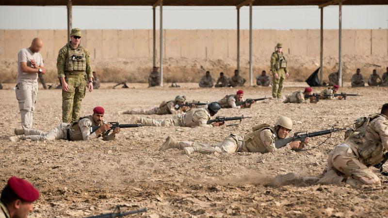 Australian Army Captain Anthony Davis, standing, instructs Iraqi soldiers, lying down with weapons, at the Taji Military Complex's Non-Commissioned Officer Academy as they practise fire and movement towards a notional enemy position at the Taji Military Complex, Iraq.