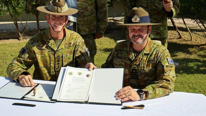 Colonel Scottie Morris, seated at a table with Captain Brett Westcott signs over command of ADF's Headquarters Middle East., during the transfer of authority on 9 December 2024.