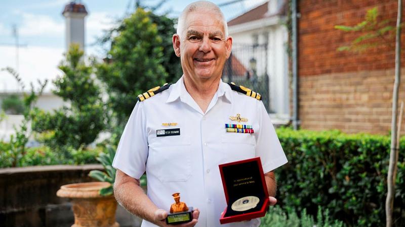Commander Peter Teichmann, in white Navy uniform, holds two awards during his retirement ceremony at HMAS Kuttabul in Sydney, New South Wales.