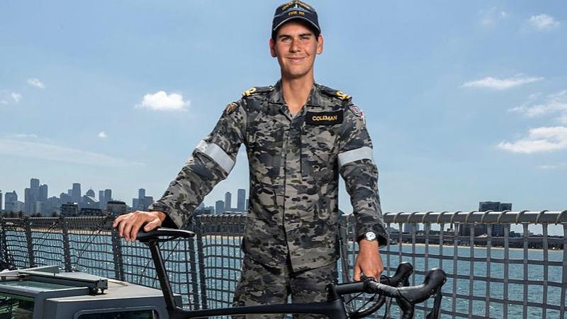 Sub-Lieutenant Gus Coleman holds with his racing bicycle on board HMAS Arunta during the ship's Navy Week 2025 open day, with the Port of Melbourne in the background.