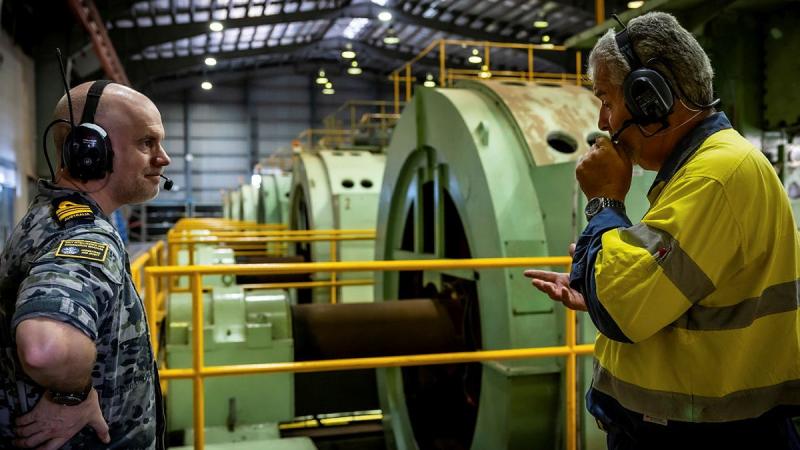 Lieutenant Commander Heath Crawford speaks with maritime and strategic communications systems engineering manager Sorin Lupulescu inside the power generation room at Harold E. Holt.