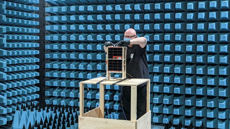 DSTG Engineer Darin Roberts attaches a radio frequency cable to the engineering model spacecraft during anechoic chamber testing at REDARC Defence & Space.