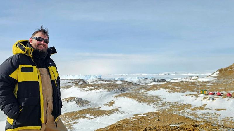 Royal Australian Navy Petty Officer Scott Thomas, from the Maritime Geospatial Warfare Unit, standing next to Australian Antarctic Program field site Law Base, Antarctica.