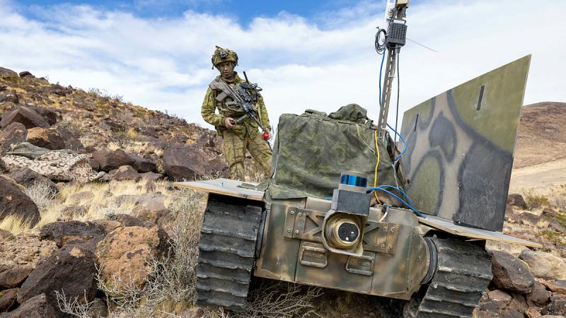 An Australian Army soldier with an uncrewed ground vehicle equipped with a prototype communications system and experimental drone launcher during Project Convergence Capstone 5 at Fort Irwin, California.