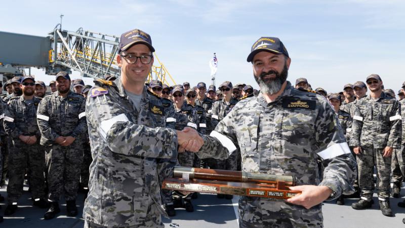 Outgoing Commanding Officer HMAS Toowoomba, Commander Barton Harrington, left, hands over the weight of command in the form of the nautical telescope to incoming Commanding Officer, Commander Adam Stafford, at HMAS Coonawarra in Darwin, NT.