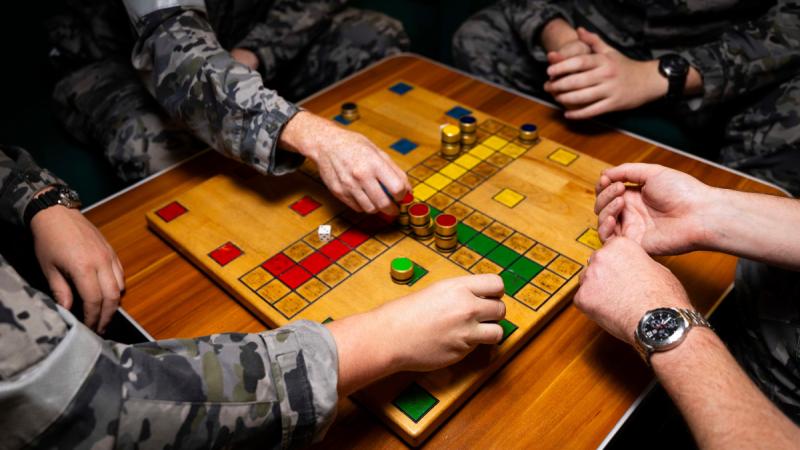 The crew of HMAS Sydney engage in one of their favorite pastimes, a game of Uckers, which parallels their voyage through the regional deployment.