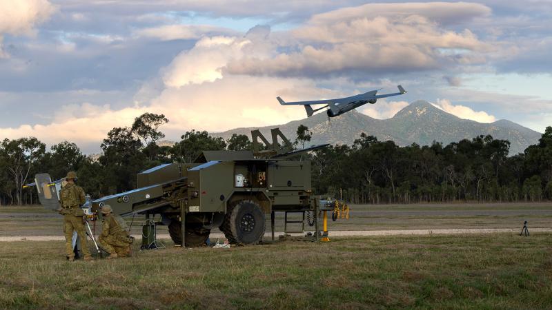 Two Australian soldiers launch a grey coloured Tactical Uncrewed Aerial System (TUAS) against a backdrop of Australian bush at Shoalwater Bay Training Area.