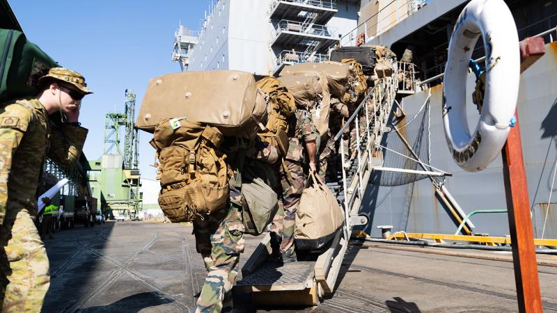 French Armed Forces personnel climb stairs to embark a Navy ship at port. 