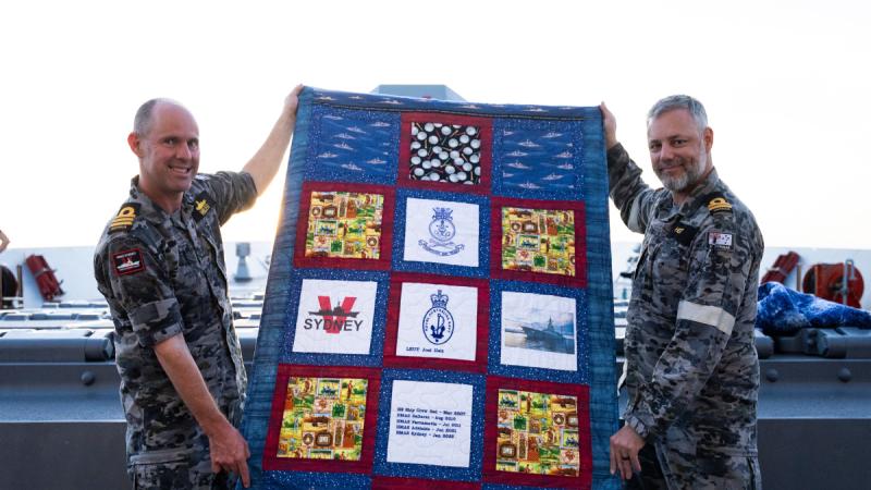Commanding Officer HMAS Sydney, Commander Ben Weller, and Lieutenant Joel Heit hold his quilt gifted by Aussie Heroes Quilts during Regional Presence Deployment 25-2.