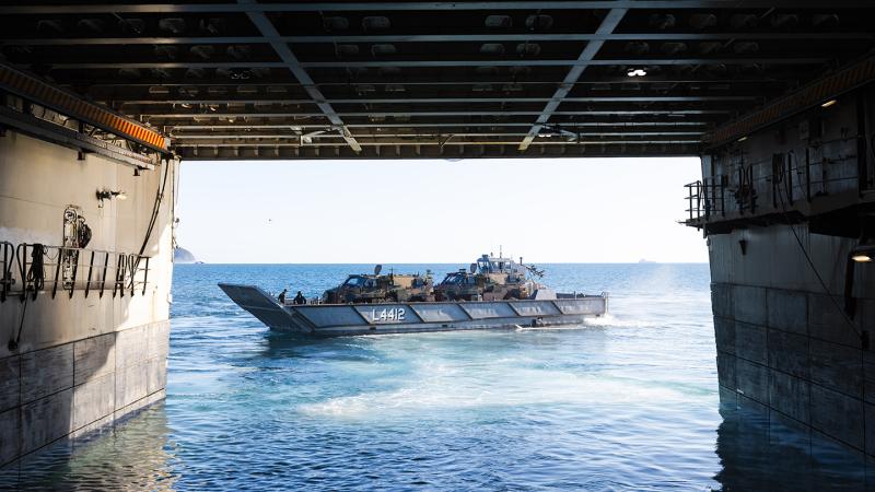 A grey Light Landing Craft carrying military vehicles transiting across the ocean from HMAS Canberra.