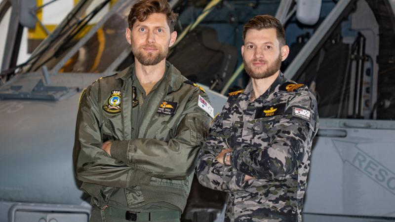 Two Navy personnel stand in front of a helicopter.