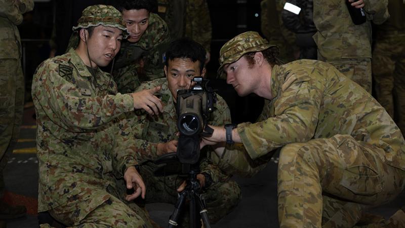 Japanese and Australian military personnel inspect a weapon. 