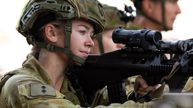 Soldier holding gun looks through gun sight.