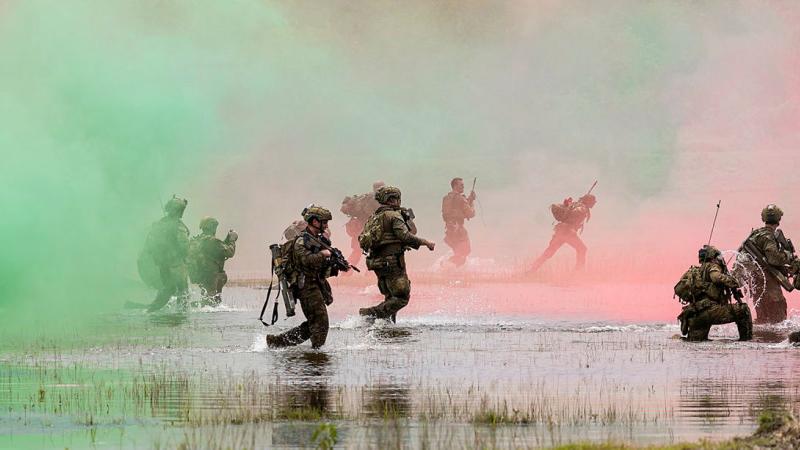 Soldiers run through a swamp with weapons drawn and coloured smoke swirling around them.