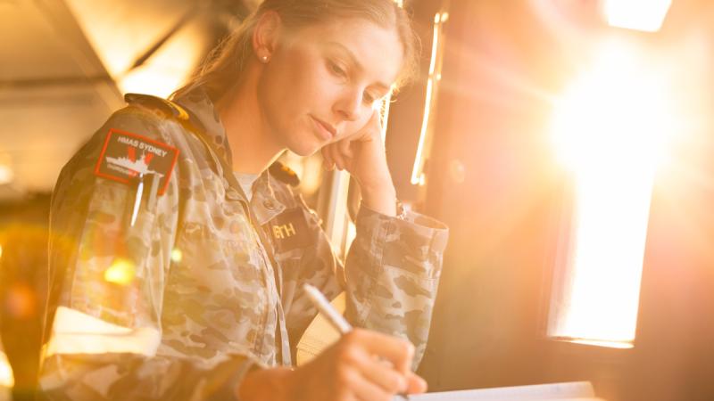 A Navy office looks deep in thought while writing.