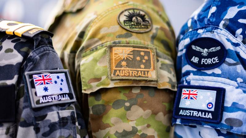 A close-up shoulders of members of Navy, Army and Air Force members standing closely together, with the Australian flag visible.