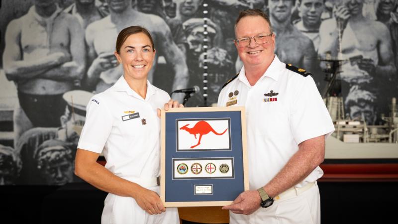 A woman and a man in Navy uniforms holding a plaque. 
