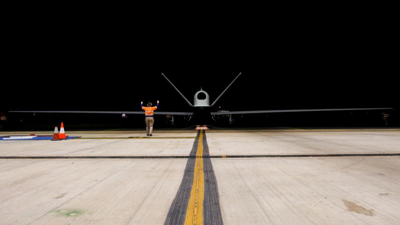 The MQ-4C is guided into the aircraft hangar by a crew member.