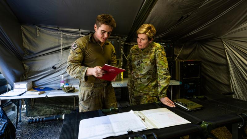 A soldier briefs a senior officer in a tent during a major exercise.