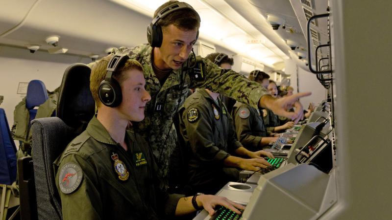 An Australian aviator and a US Navy officer work at a computer console on board a military aircraft.  