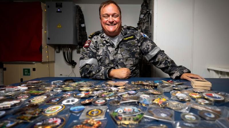 Leading Seaman Hamburger sitting behind a table covered in collectable coins.