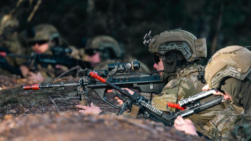 Four cadets, lying down at the top of an incline, readying weapons.