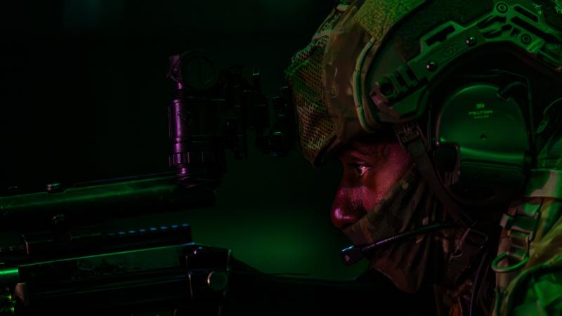 A photo of a cadet in a helmet looking down their gunsight during a nighttime exercise.