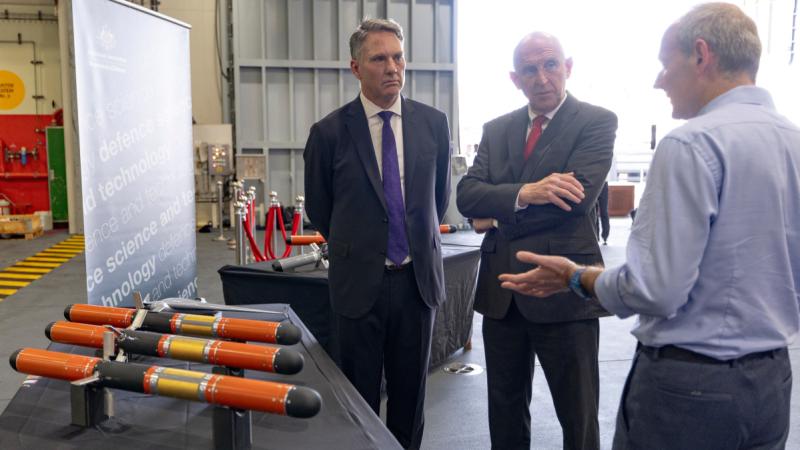 Three men talking at looking at a display of Defence Science and Technology Group products.