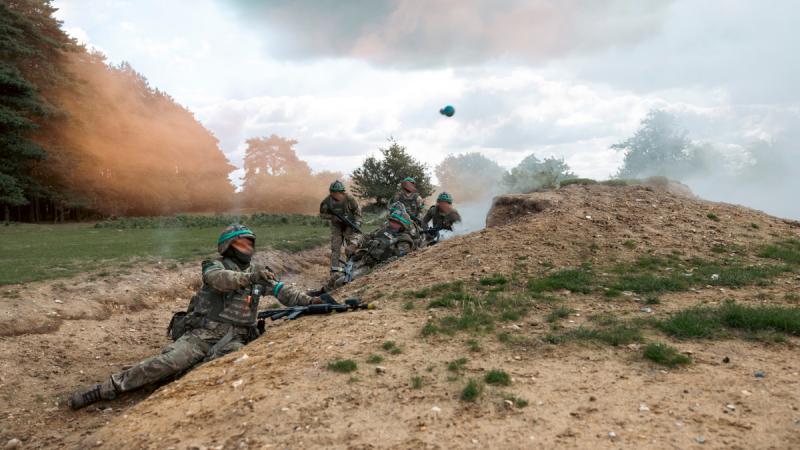 A soldier throws a grenade while he and others assault a trench during Operation Kudu